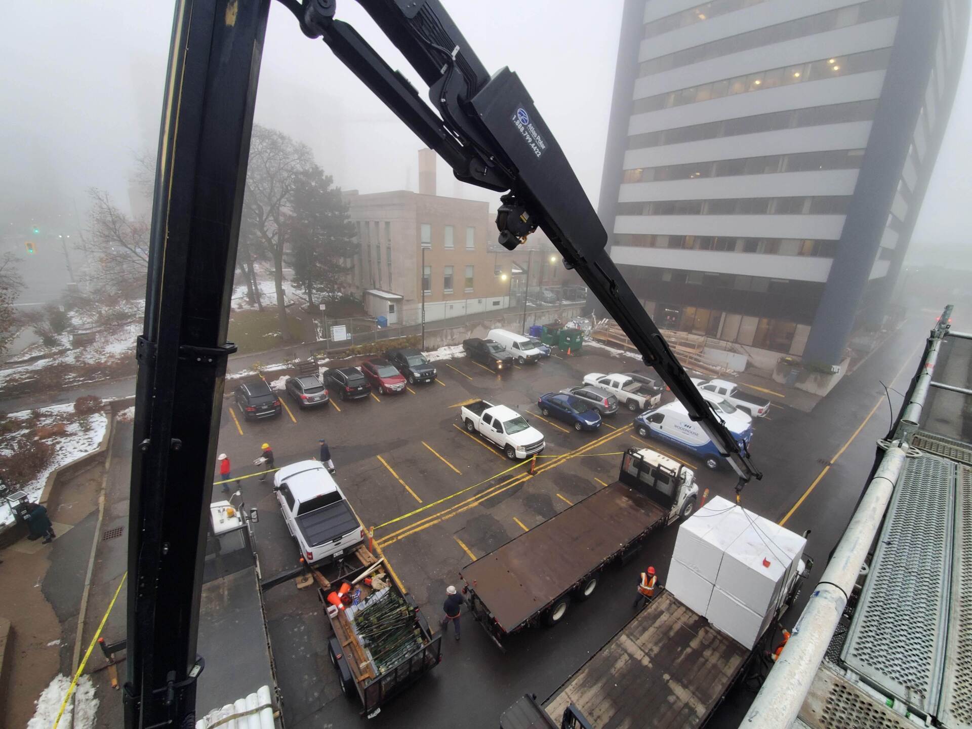 An elevated view from a crane shows a foggy street scene with people and vehicles around a parking lot near buildings.