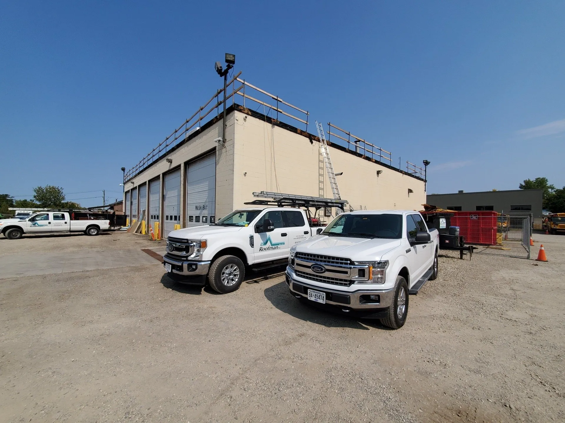 This image features an industrial setting with two white pickup trucks parked in front of a beige warehouse with multiple garage doors and a clear blue sky.