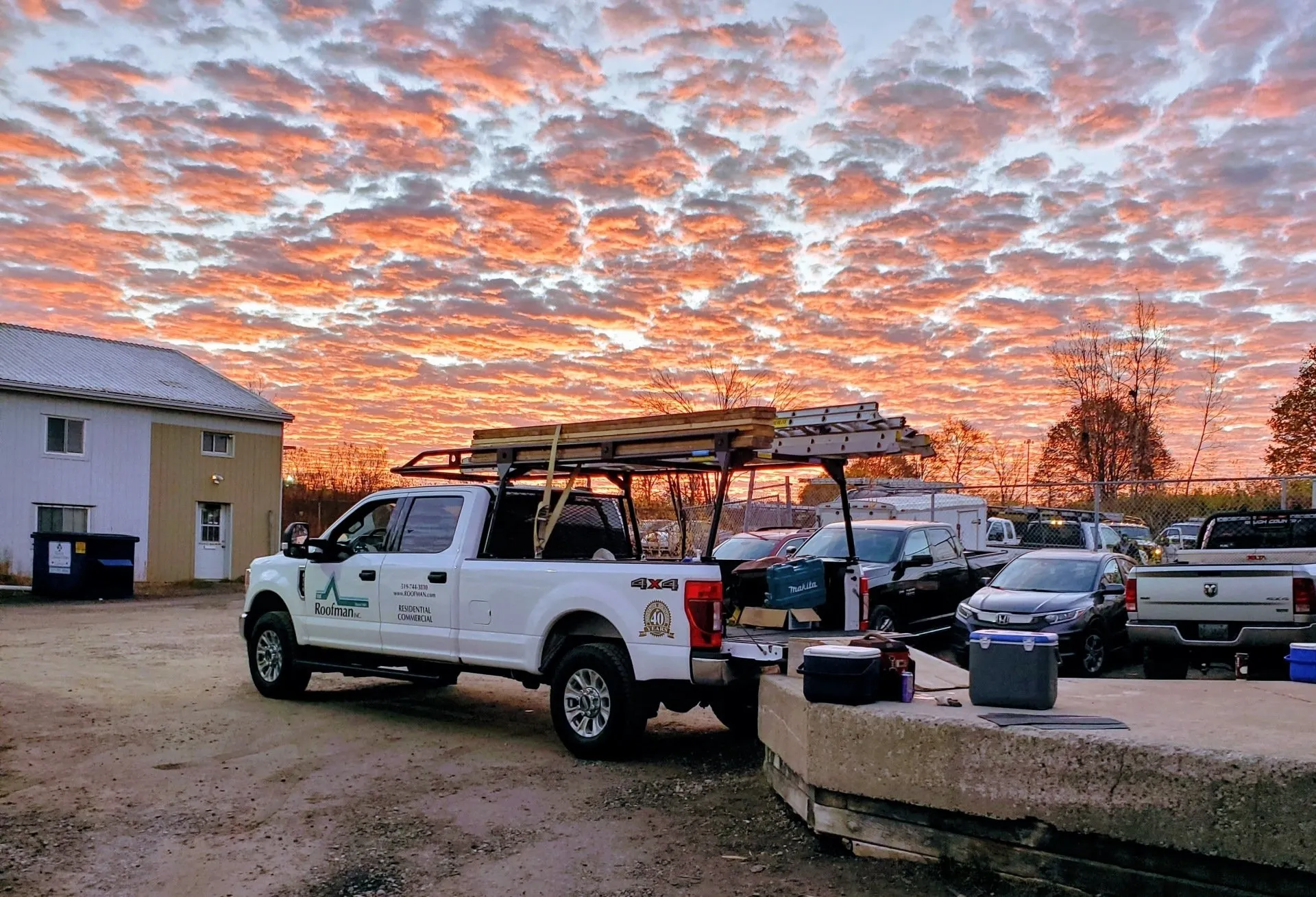 A vibrant sunrise with fiery clouds over a parking lot with a pickup truck loaded with construction materials in the foreground.