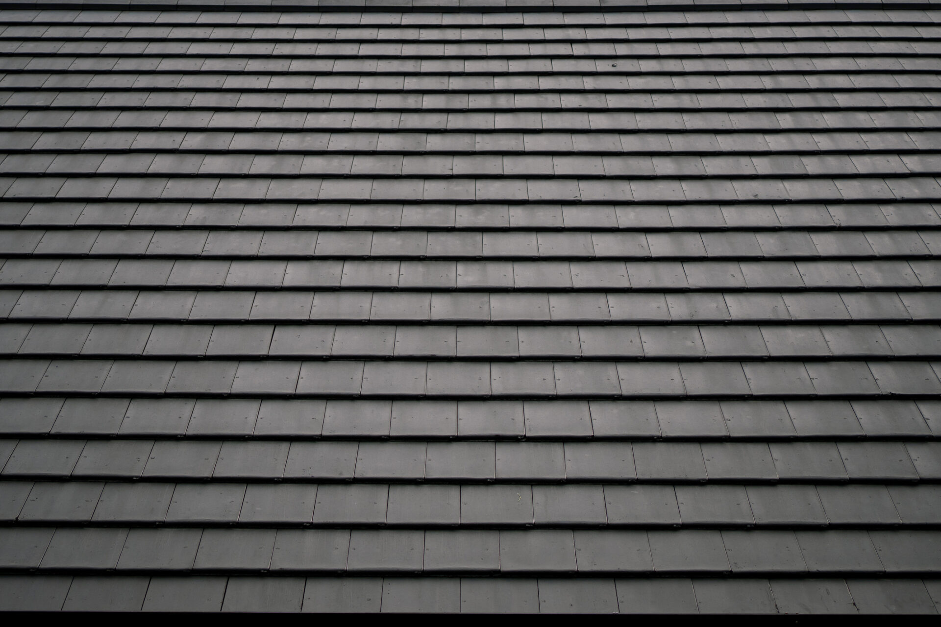 The image shows a close-up view of a dark slate roof with a regular pattern of overlapping rectangular tiles, creating a textured architectural surface.