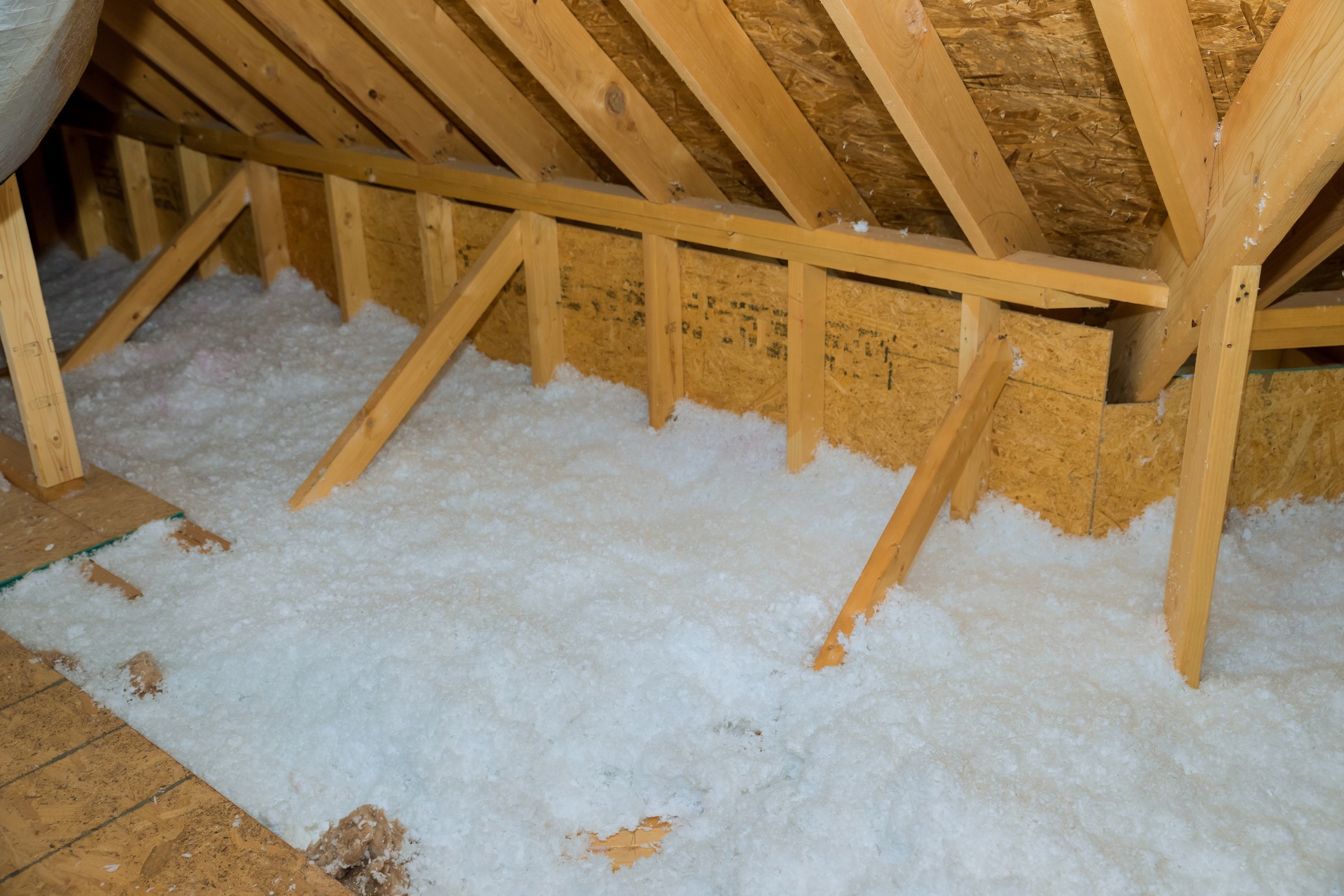 An attic space with wooden trusses and a floor partially covered in fluffy, white insulation material, alongside OSB (oriented strand board) panels.
