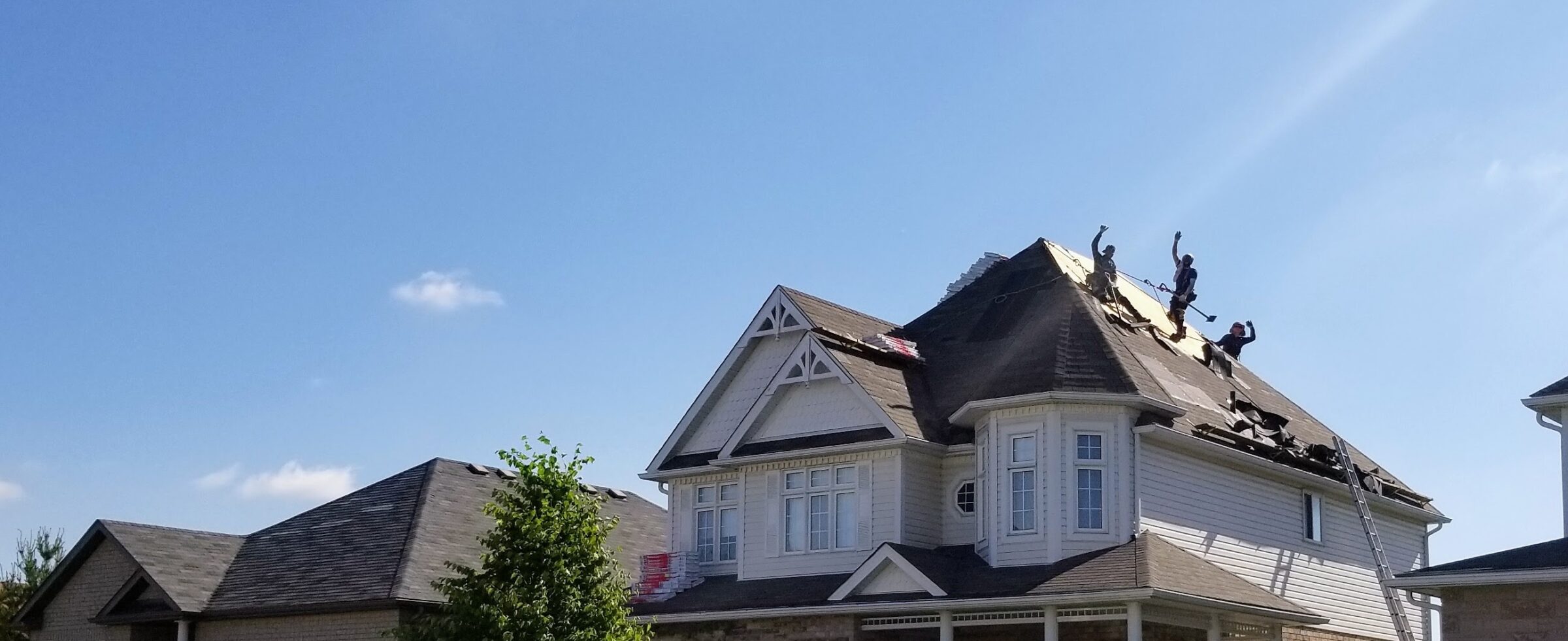 A residential house under renovation with persons working on the partially removed roof against a clear blue sky with bright sunlight.