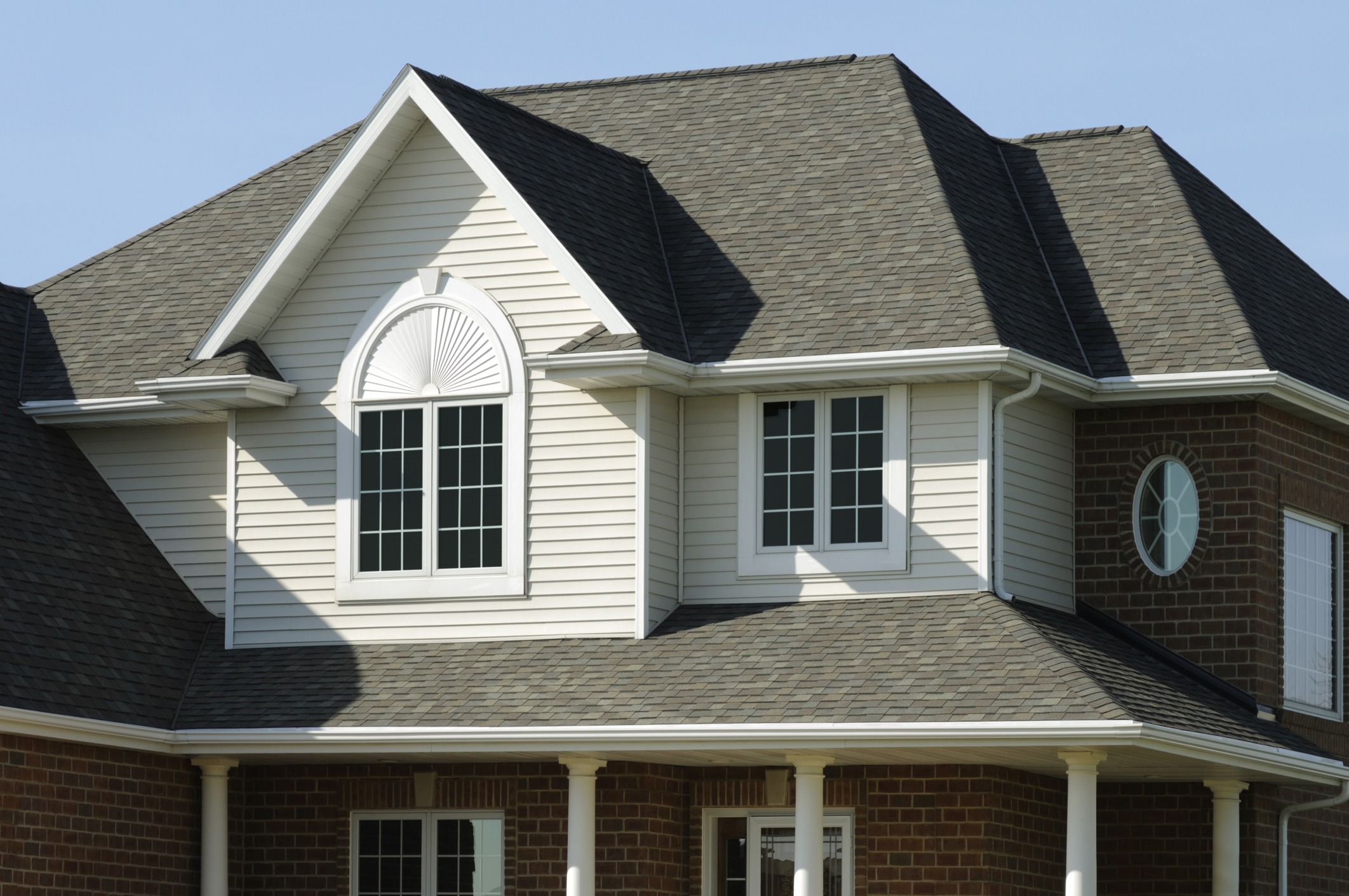 This image shows the upper facade of a two-story suburban house with a shingled roof, brick accents, white siding, and multiple windows.