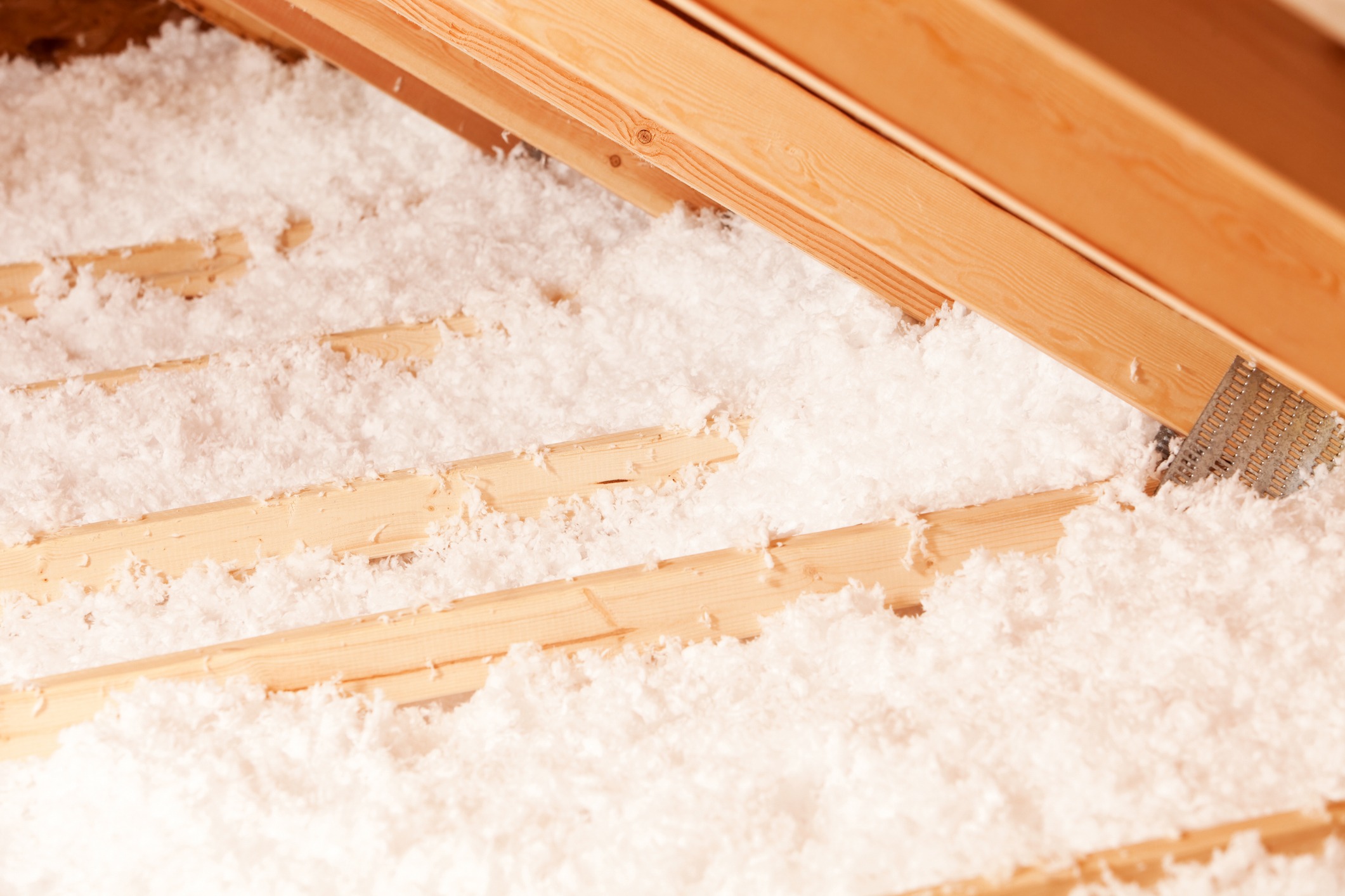 The image shows a wooden attic with fluffy, white insulation material between the beams, suggesting a focus on energy efficiency and thermal regulation.