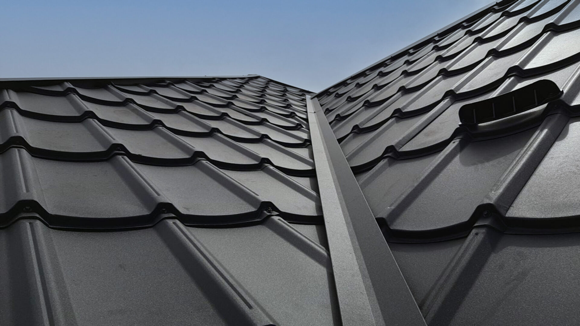 The image showcases a close-up view of a textured metal roof with wavy patterns and a vent under a clear blue sky.