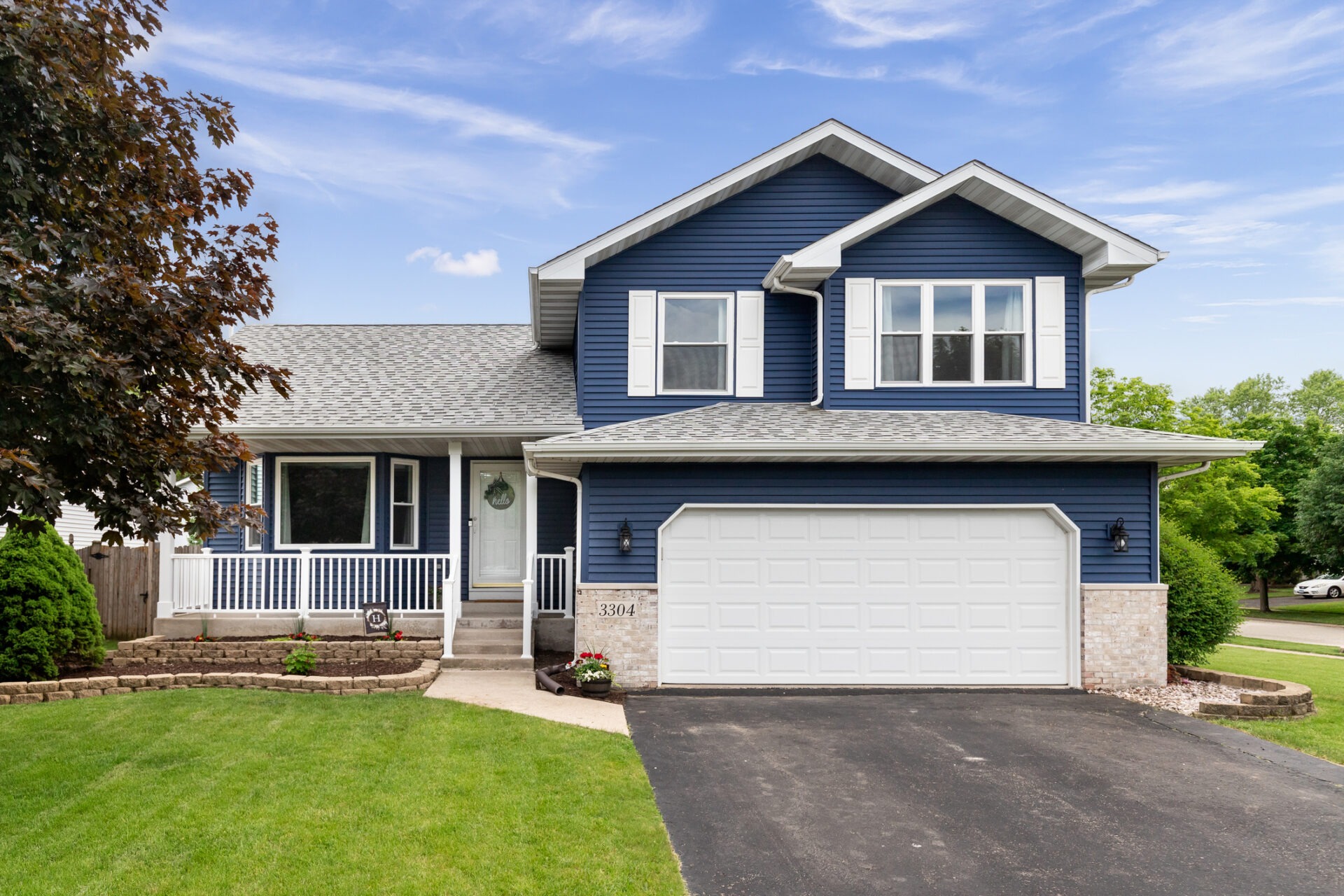 This is a suburban house with a blue facade, white garage door, neat lawn, and a paved driveway under a clear sky.