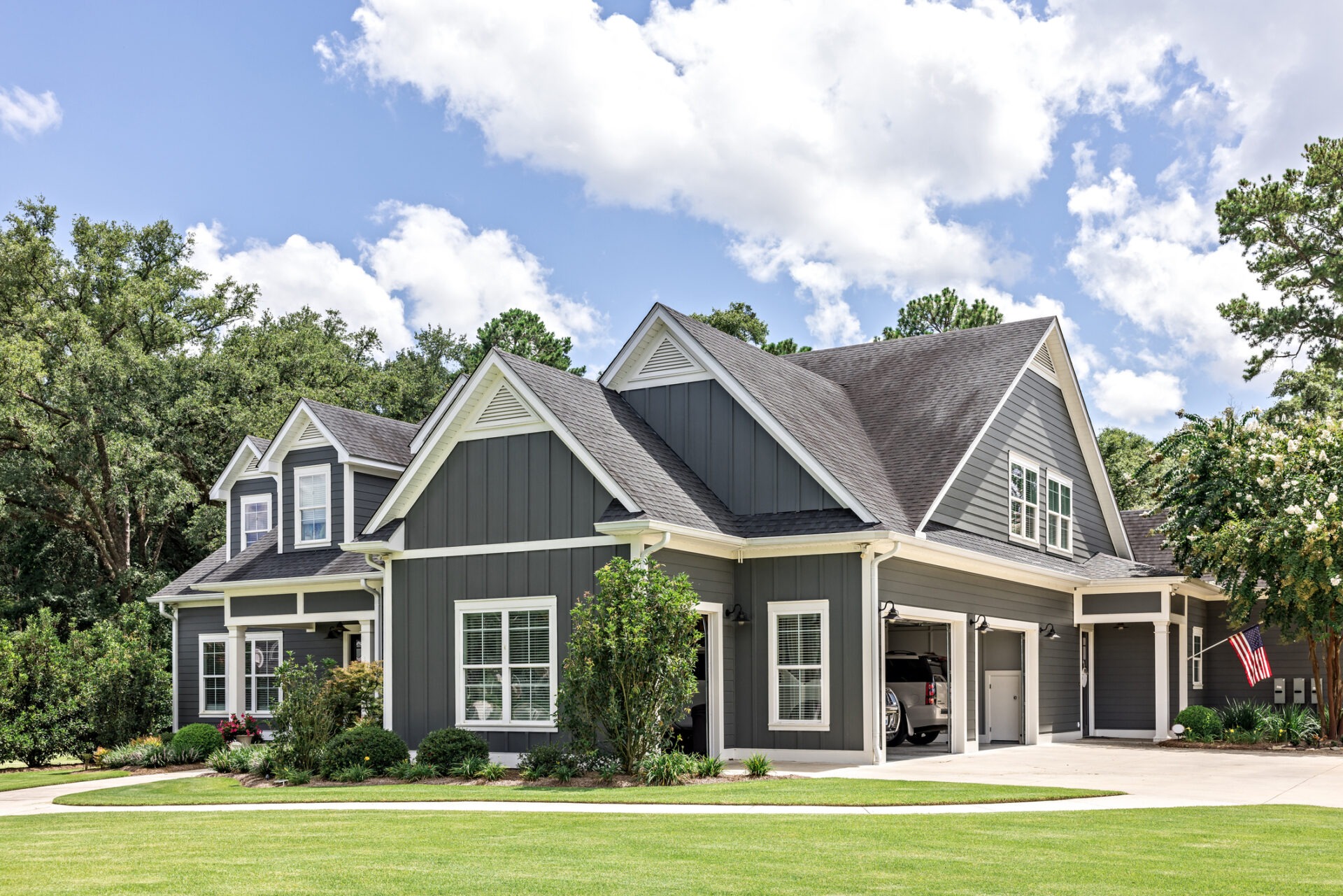 A modern two-story house with gray siding, white trim, a covered porch, an attached garage, lush green lawn, and an American flag displayed.