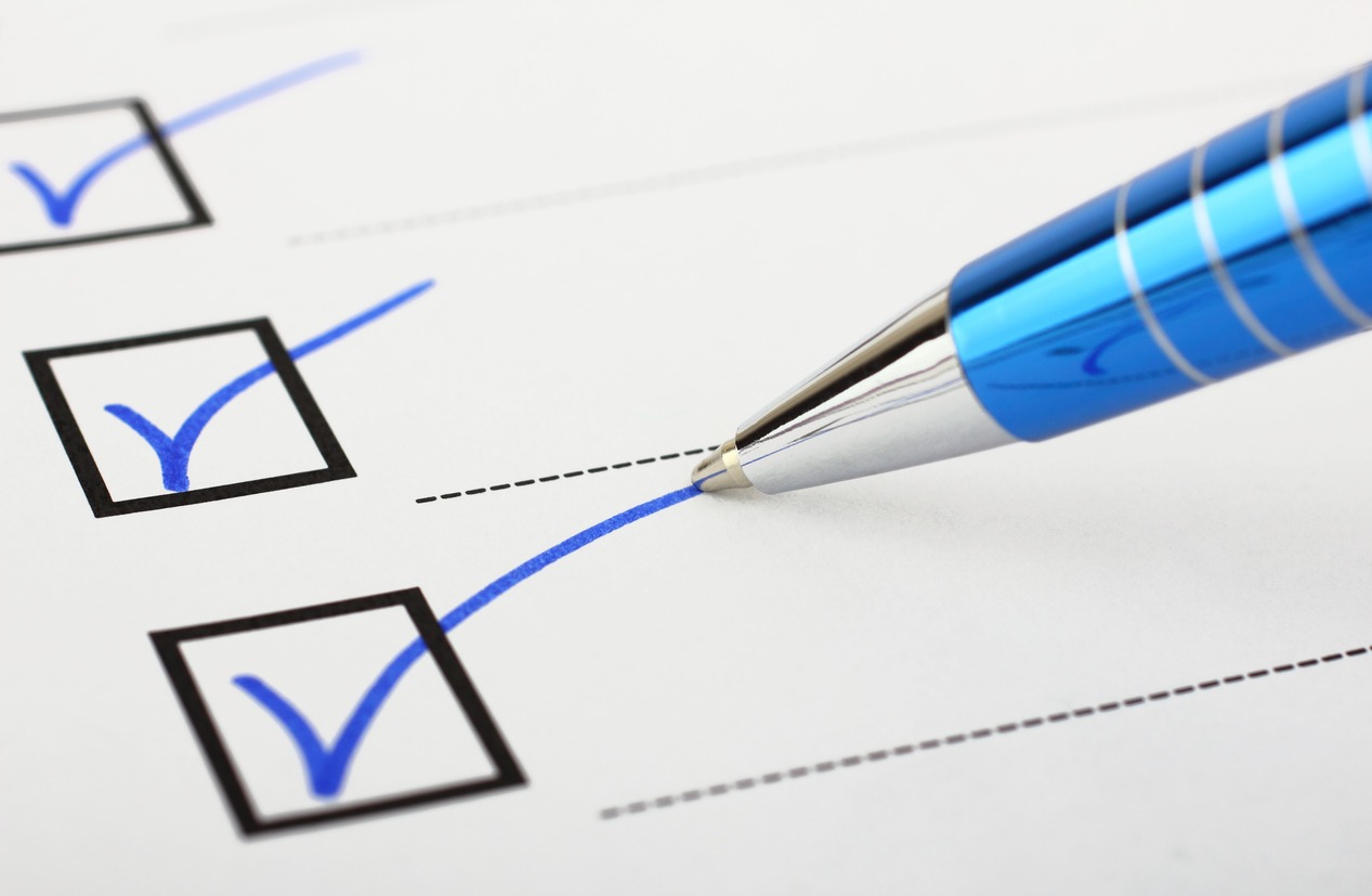 A close-up of a blue ballpoint pen next to check marks in black outlined boxes on a white checklist paper.