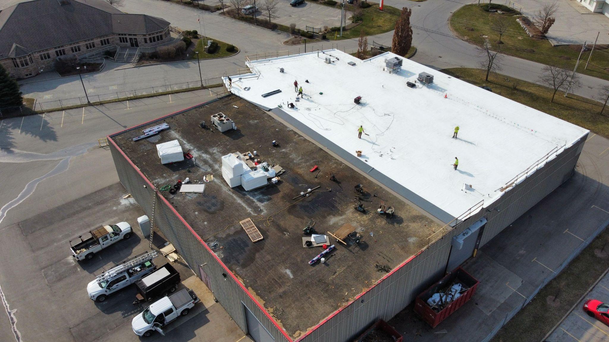 Aerial view of a large commercial roof during a TPO membrane installation using the RhinoBond attachment system. Workers and construction equipment are visible across the partially completed roof.