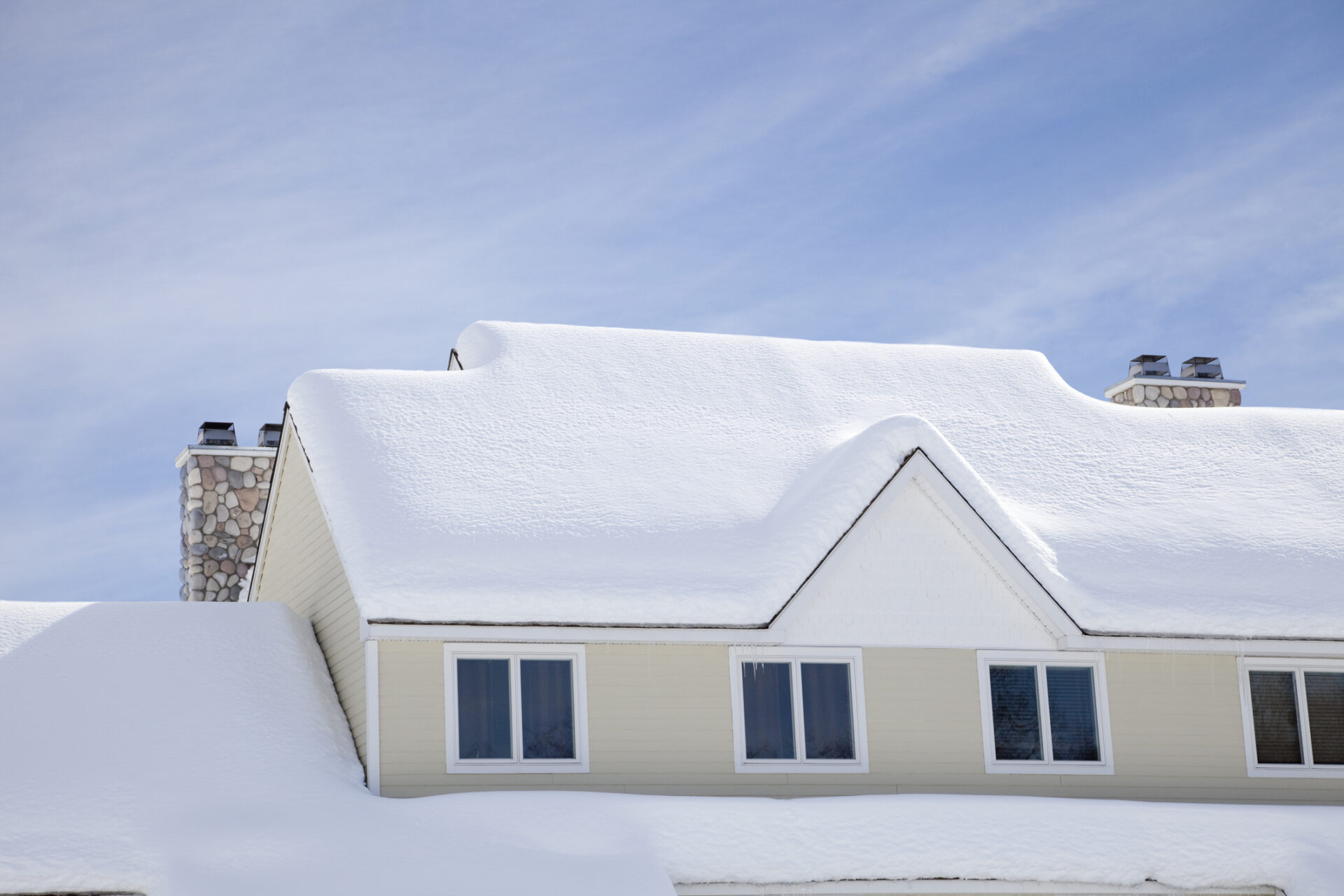 Snow-covered house roof with icicles, stone chimney, and bright blue sky, creates a serene winter scene. No people or landmarks visible.