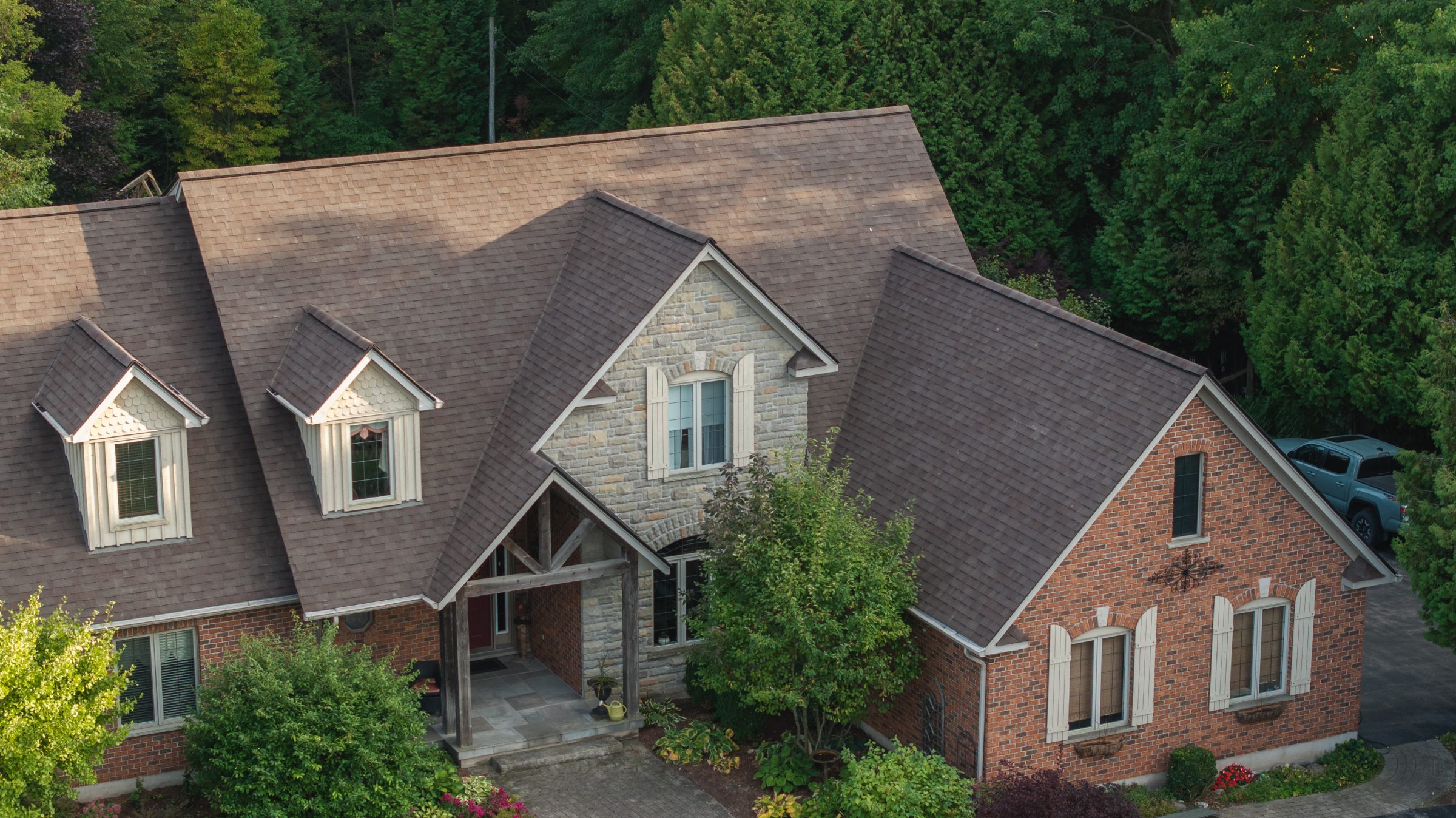 View of red brick home with brown shingle roof at sunset in the summer.