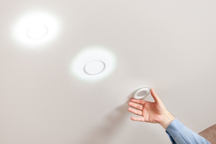 Person adjusting white pot lights in a white ceilng