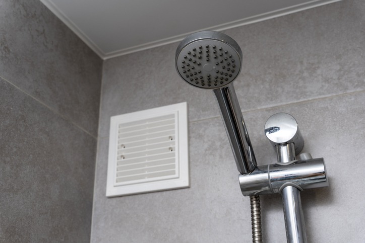 Air vent in a bathroom, on a tile wall next to a shower head