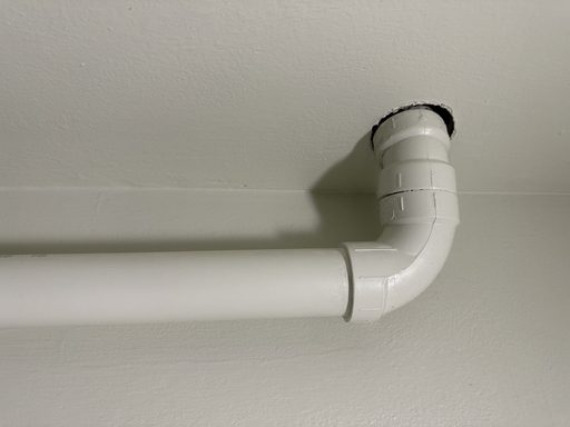 White PVC plumbing tube with an elbow bend going into a ceiling