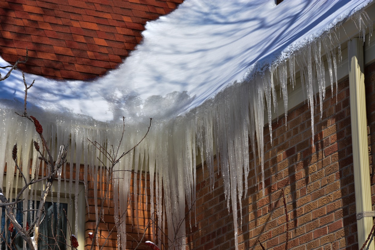 Ice buildup in roof gutters from melting snow on a sunny day